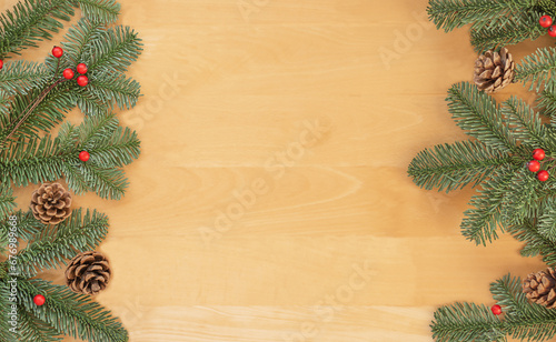 Christmas flat lay of green fir branches, red berries and brown cones on wooden background.