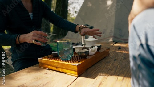 The hands of a professional tea master who pours fresh natural green tea from a glass teapot into bowls on wooden chaban table photo