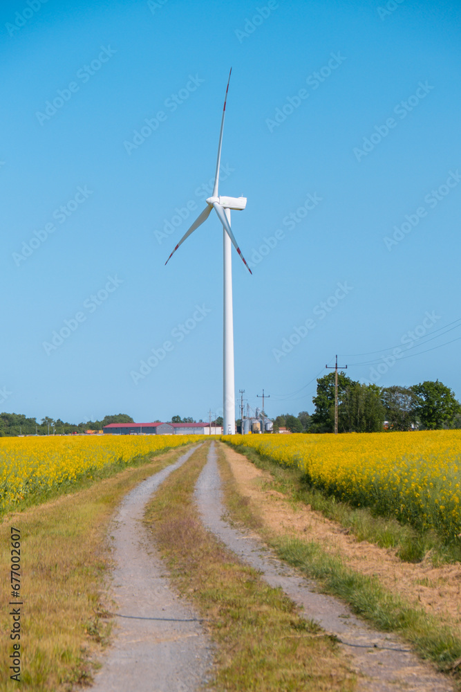 Wind turbine on grassy yellow field against cloudy blue sky in rural area during sunset. Offshore windmill park with stormy clouds in farmland Poland Europe. Wind power plant generating electricity Wind turbine on grassy yellow field against cloudy blue sky in rural area during sunset. Offshore windmill park with stormy clouds in farmland Poland Europe. Wind power plant generating electricity