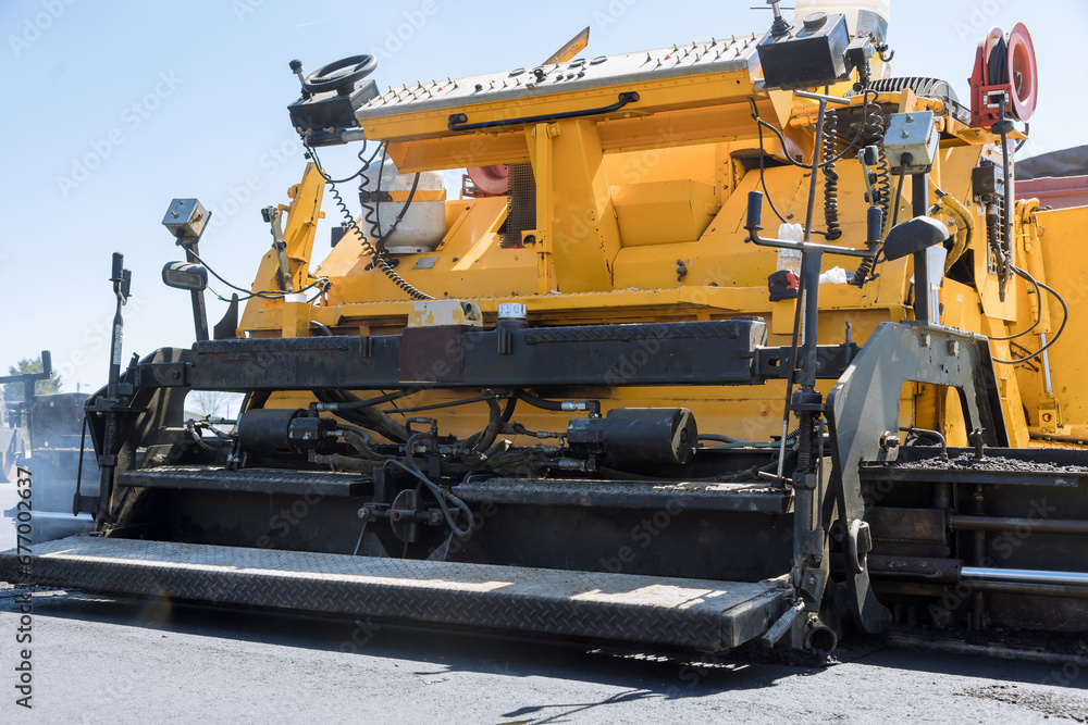 During highway construction, pavement machine lays fresh bitumen asphalt over gravel base