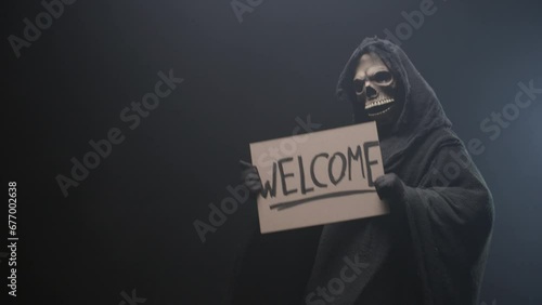 Grim reaper holding a Welcome sign and luring people to him, dancing, on the black background. Mysticism and the afterlife.