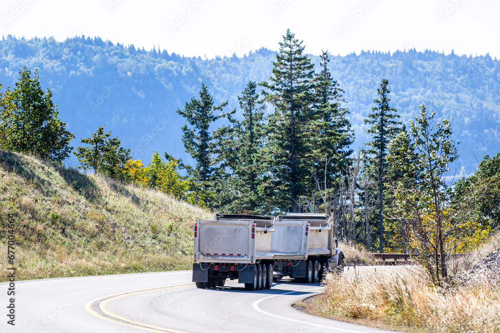 Heavy duty big rig tipper semi truck with two tip trailers running on the mountain winding road going to work side for next load