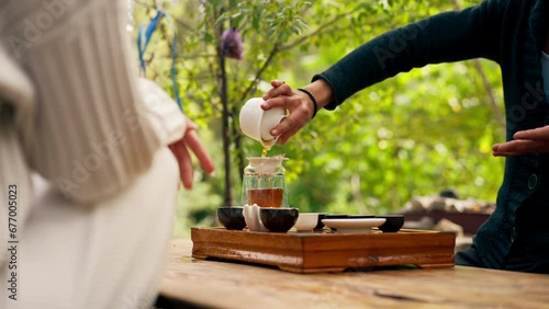 close-up The hands of a professional tea master who pours fresh natural green tea from a glass teapot into bowls on wooden chaban table photo