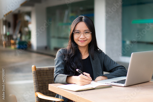 Asian businesswoman sitting happily with her laptop and takes notes intensely and smiles