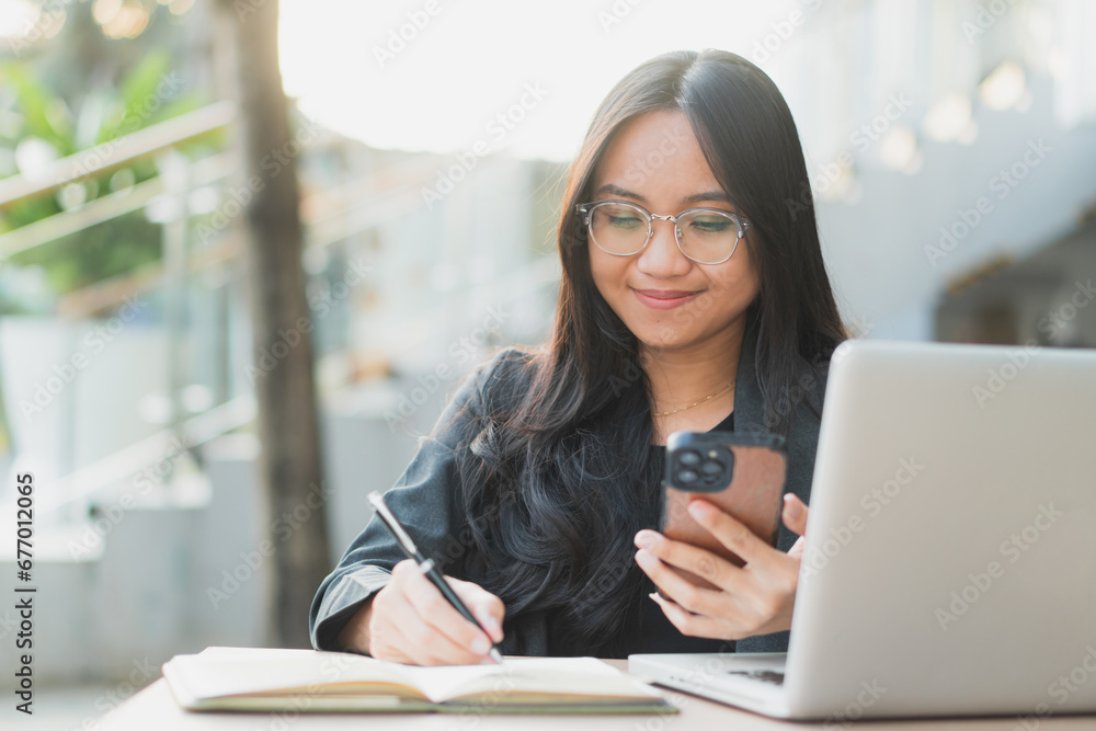 Young confident businesswoman using her smart phone while sitting at the office desk. Young confident businesswoman using her smart phone while sitting at the office desk.
