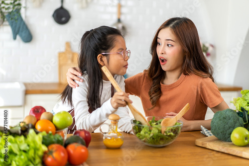Portrait of enjoy happy love asian family mother and little asian girl daughter child having fun help cooking food healthy eat together with fresh vegetable salad and ingredient in kitchen.