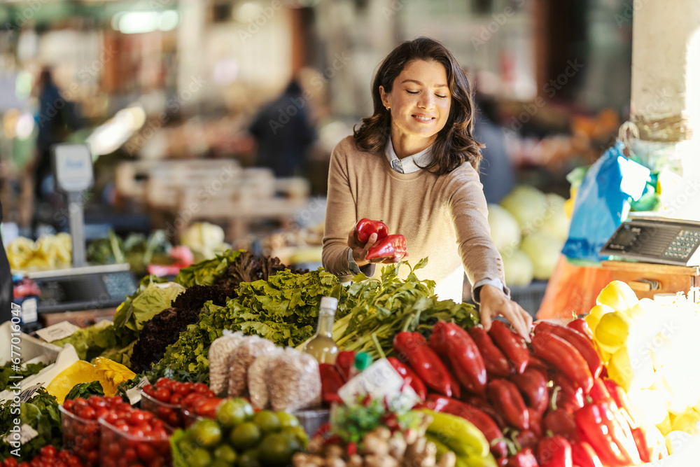 A happy woman is choosing vegetables on stand on farmers market.