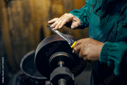 Bild auf Leinwand Cropped picture of craftsman's hands sharpening knife in his workshop