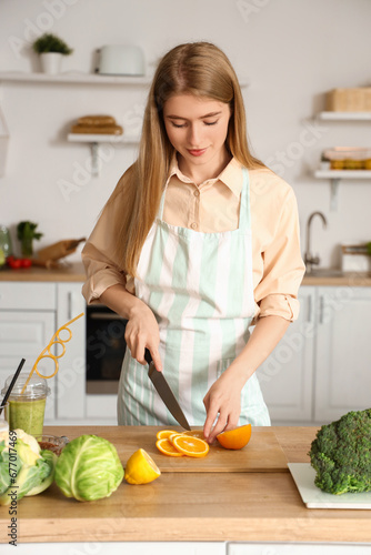 Young woman cutting orange in kitchen