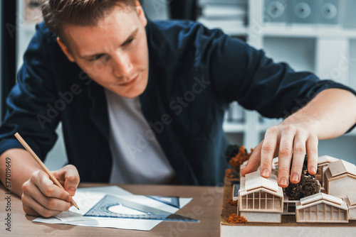 Architect designer studies elegant house model, reviewing structure design for improvement with construction plan on table. Creativity and innovation in architectural design. Iteration