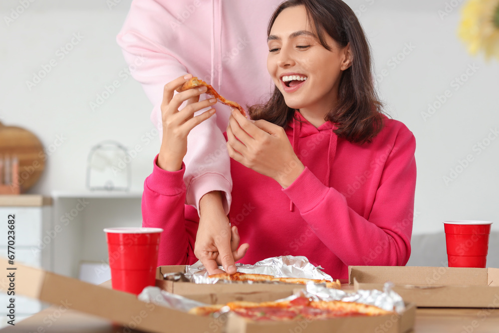 Young couple eating tasty pepperoni pizza in kitchen Young couple eating tasty pepperoni pizza in kitchen