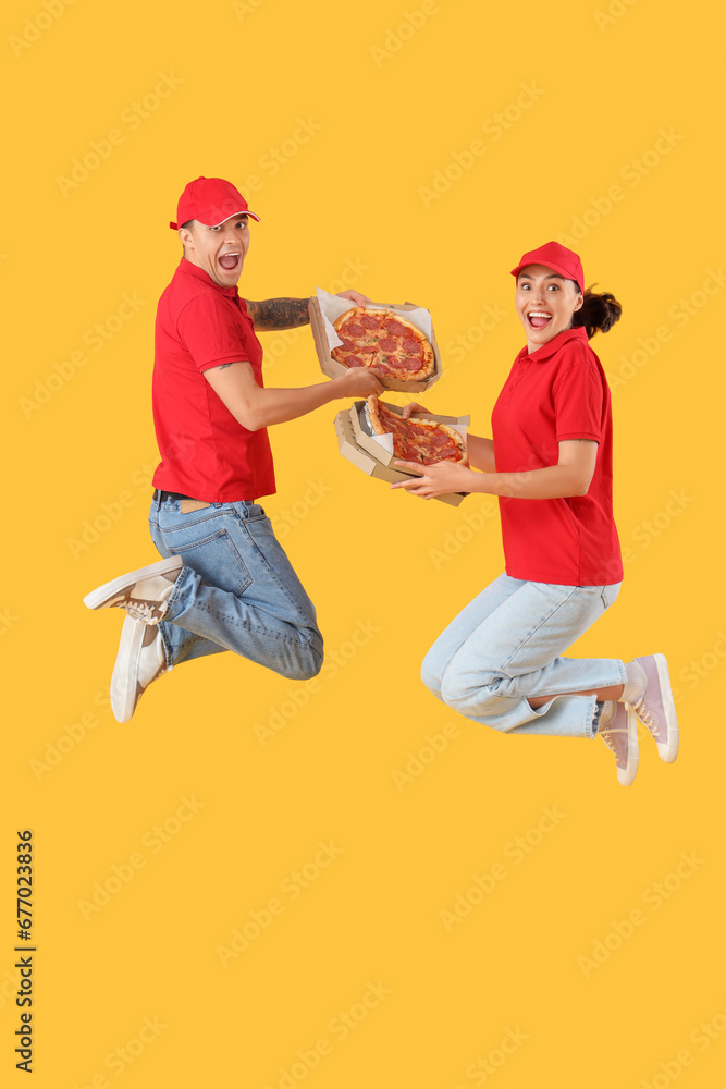 Fototapeta premium Young couriers with tasty pepperoni pizza jumping on yellow background