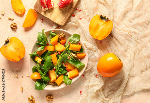 Bowl of delicious salad with persimmon, pomegranate seeds and walnut on beige background