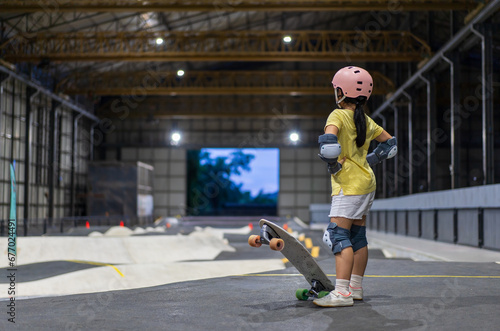 asian child skater or kid girl start riding surf skate at indoor pump track or fun playing skateboard in skate park by extreme sports surfing to wearing helmet elbow pads wrist knee guard body safety photo