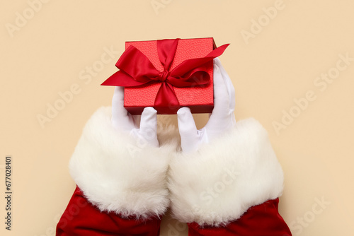Santa Claus with red gift box on beige background © Pixel-Shot
