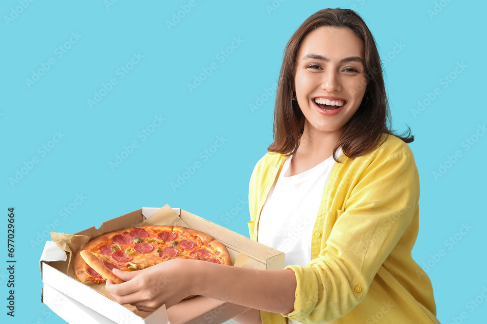 Young woman holding cardboard box with tasty pizza on blue background Young woman holding cardboard box with tasty pizza on blue background