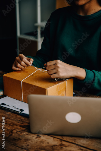 Startup small business entrepreneur or freelance Asian woman using a laptop with box, Young success Asian woman with her hand lift up, online marketing packaging box and delivery, SME concept. © ARMMY PICCA