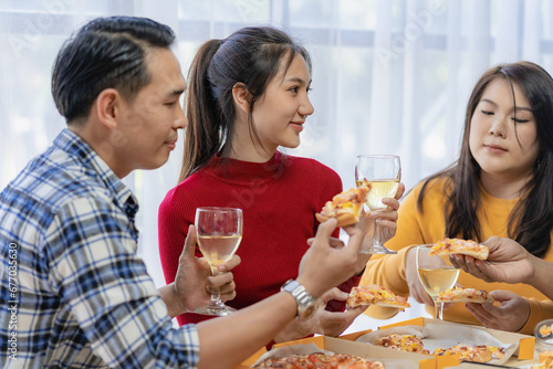 Group of happy Asian young people with friends celebrate clinking glasses during party, food, pizza, snacks with silverware Stemware glass and delicious food