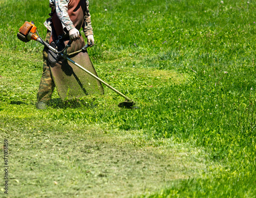 A man mows green grass with a petrol trimmer