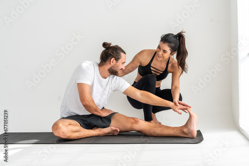 Healthy lifestyle concept. A woman is a trainer teaching yoga poses and stretching the arms and legs to male students practicing exercise on a yoga mat at the studio.