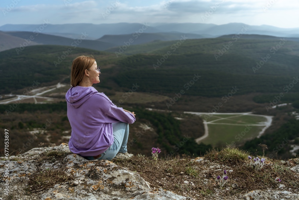 Naklejka premium Girl on mountain peak looking at beautiful mountain valley in fog at sunset in summer. Landscape with sporty young woman, foggy hills, forest, sky. Travel and tourism, hiking