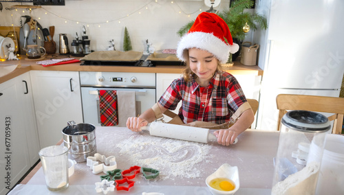 Daughter learning to cook, rolls out the dough with a rolling pin, helps in the white kitchen and cookies for Christmas and new year. 