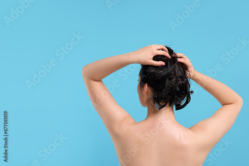 Woman washing hair on light blue background, back view. Space for text