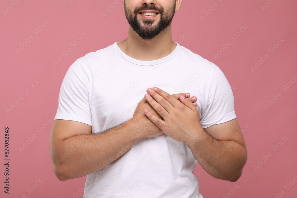 Thank you gesture. Grateful man holding hands near heart pink background, closeup Thank you gesture. Grateful man holding hands near heart pink background, closeup
