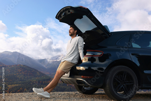 Happy man sitting in trunk of modern car in mountains #677064891