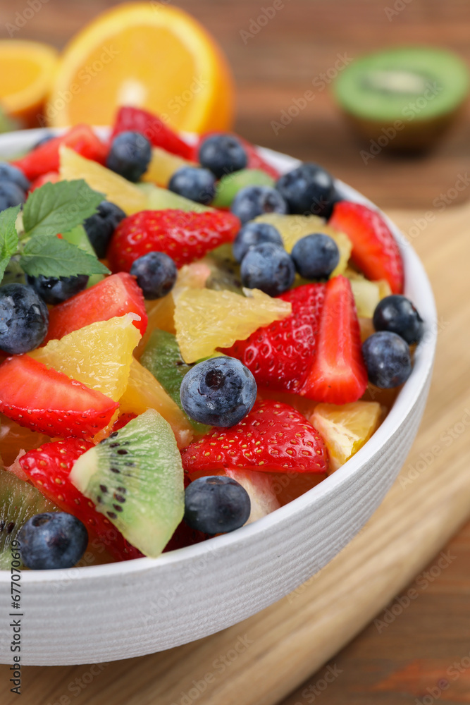 Delicious fresh fruit salad in bowl on wooden table, closeup