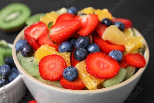 Delicious fresh fruit salad in bowl and ingredients on dark table  closeup