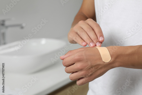 Man putting sticking plaster onto hand indoors, closeup. Space for text