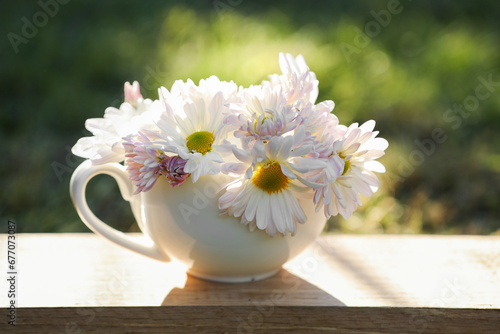 Beautiful wild flowers in cup on wooden table against blurred background, closeup