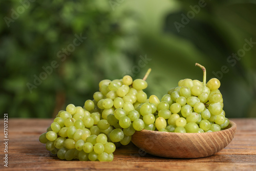 Delicious fresh green grapes on wooden table against blurred background, space for text