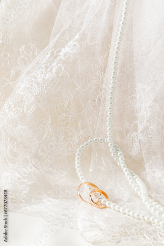 A chic wedding background for design. Antique tulle with floral ornament and a long string of pearl beads with two gold rings strung on them.