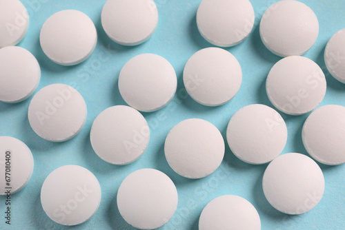 Many white pills on light blue background, flat lay