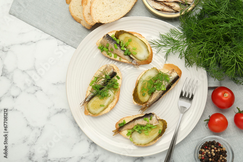 Delicious sandwiches with sprats, pickled cucumber, green onion and dill served on white marble table, flat lay. Space for text