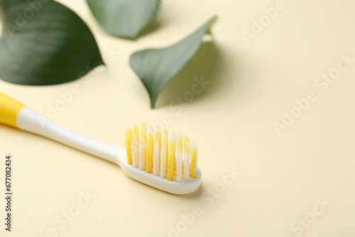 Plastic toothbrush and green leaves on pale yellow background  closeup. Space for text