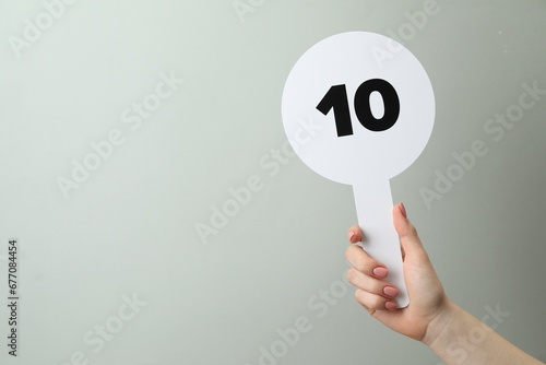Woman holding auction paddle with number 10 on light grey background, closeup. Space for text photo