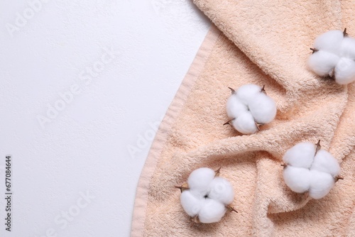 Fluffy cotton flowers and beige terry towel on white background, top view. Space for text