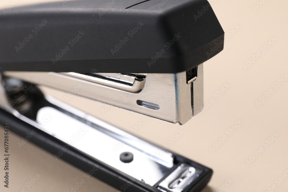 Black stapler with staples on beige background, closeup Black stapler with staples on beige background, closeup