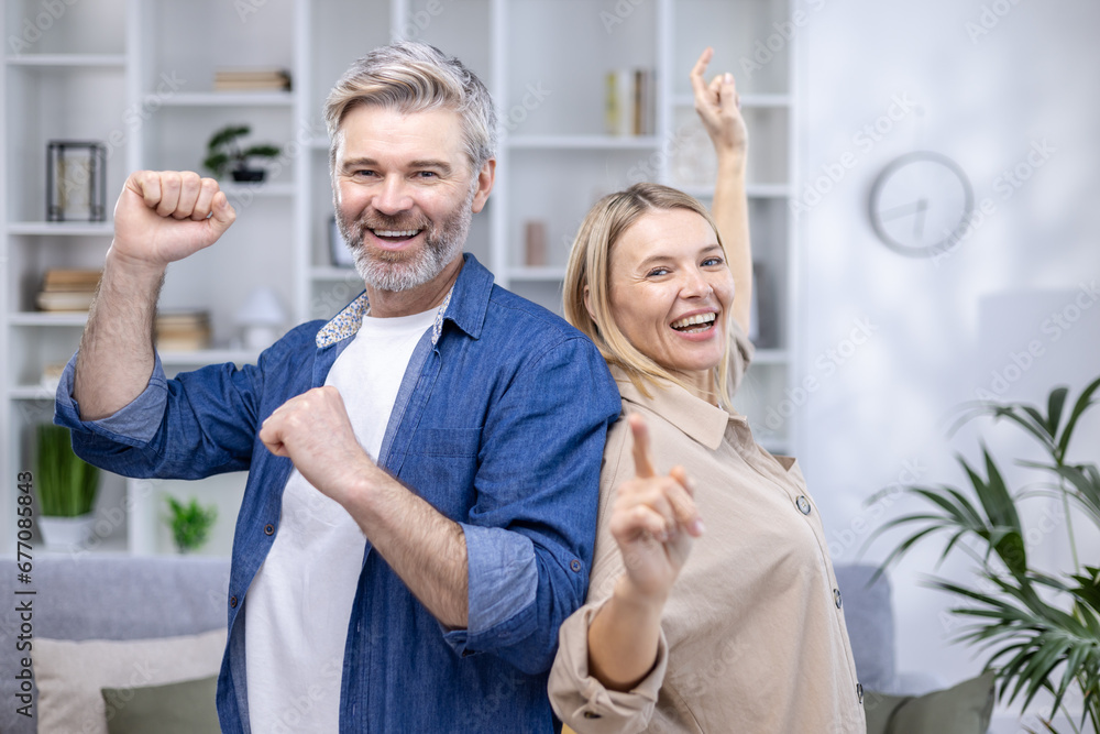 Happy senior couple dancing in their cozy living room, smiling looking at camera, happy long marriage, husband and wife spending weekend at home. Happy senior couple dancing in their cozy living room, smiling looking at camera, happy long marriage, husband and wife spending weekend at home.