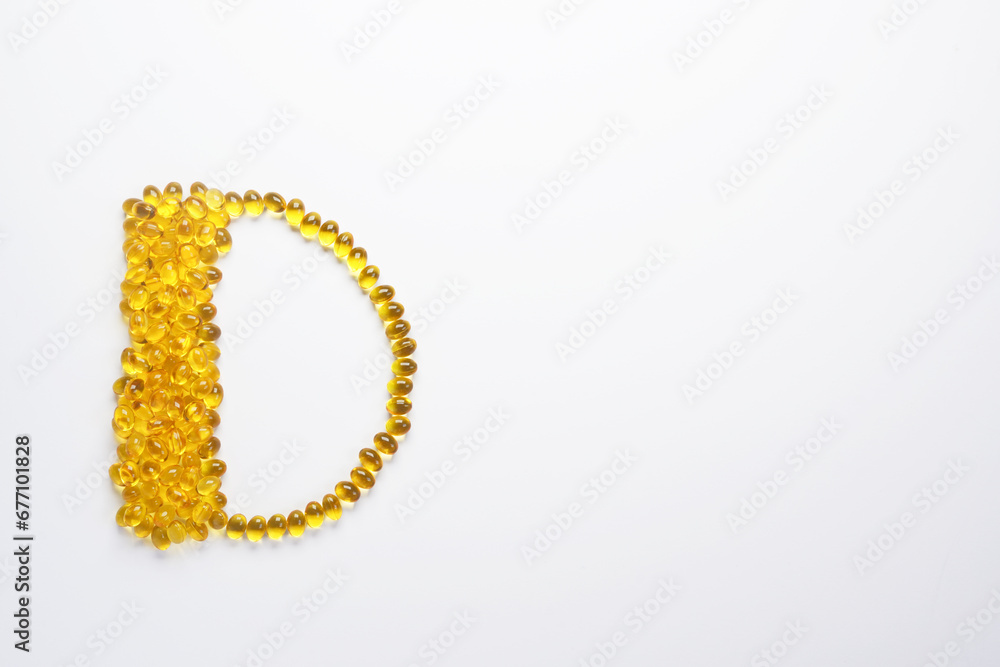 Yellow gelatin capsules in the form of the letter D on a white background. Vitamin D. Top view, flat lay. Space for text. Yellow gelatin capsules in the form of the letter D on a white background. Vitamin D. Top view, flat lay. Space for text.