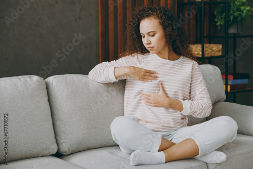 Full body young woman wearing casual clothes sits on grey sofa couch hold touch breast check health stay at home hotel flat rest relax spend free spare time in living room indoor. Healthcare concept.