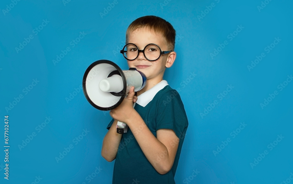 funny child on an isolated blue background shouts into megaphone to announce something, pointing ahead. Space for text. Childhood lifestyle concept funny child on an isolated blue background shouts into megaphone to announce something, pointing ahead. Space for text. Childhood lifestyle concept
