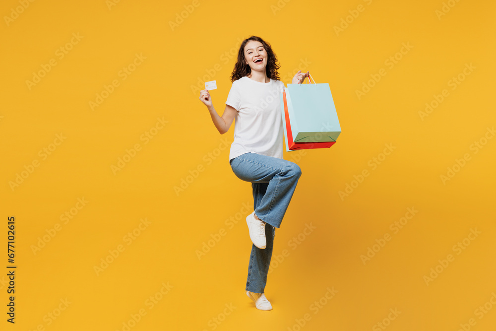 Full body young woman wears t-shirt casual clothes hold in hand paper package bags after shopping show credit bank card isolated on plain yellow orange background. Black Friday sale buy day concept. - obrazy, fototapety, plakaty 