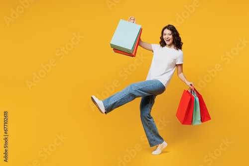 Full body satisfied young woman wears t-shirt casual clothes hold in hand paper package bags after shopping walk go isolated on plain yellow orange color background. Black Friday sale buy day concept. photo
