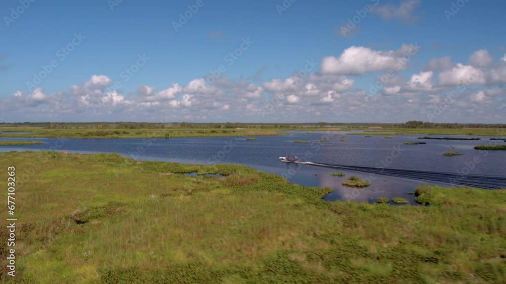 Aerial Panning Shot Of People Exploring Atchafalaya River In Motorboat, Drone Flying Over Green Landscape On Sunny Day - Bayou, Louisiana Aerial Panning Shot Of People Exploring Atchafalaya River In Motorboat, Drone Flying Over Green Landscape On Sunny Day - Bayou, Louisiana
