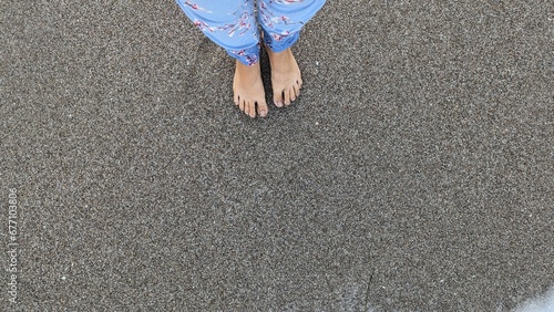 Womans's feet on the sand and a running foam wave on the beach, top down view