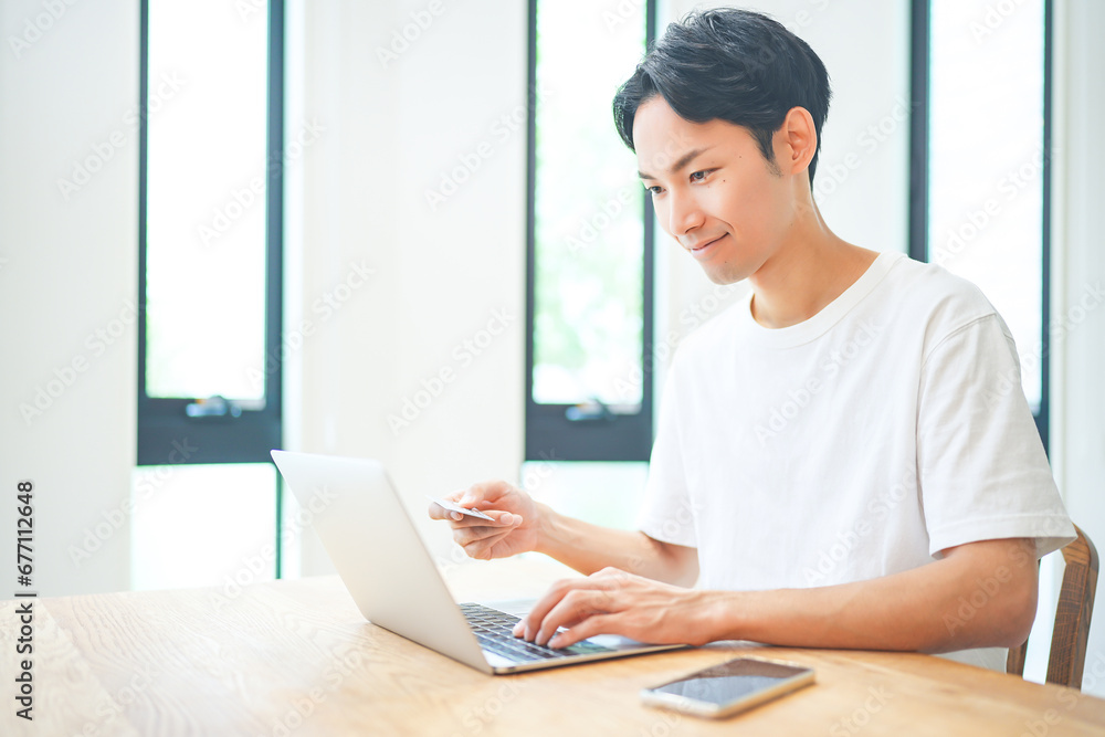 Fototapeta premium ノートパソコンでクレジットカード決済をする若い男性